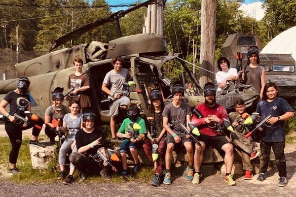 Groupe d'une dizaine de jeunes avec un accompagnateur dans leur équipement de paintball devant un vieil hélicoptère